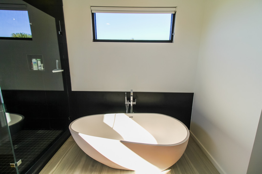 Slipper tub with floor mounted tub filler and black wall tile 12 x 24 runs into the adjacent shower.